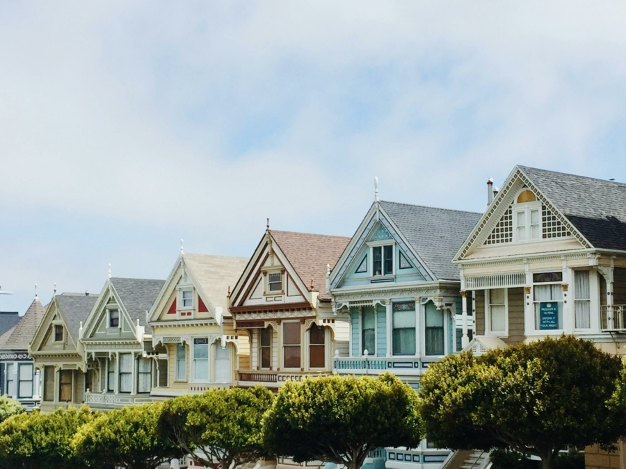A row of colorful houses with different architectural styles, lined up side-by-side. There are trees with green leaves in front of the houses.