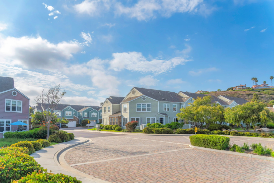 A row of colorful houses with green lawns on a sunny day. There is a sidewalk in front of the houses with trees lining the street. This is a typical scene in a suburban neighborhood.
